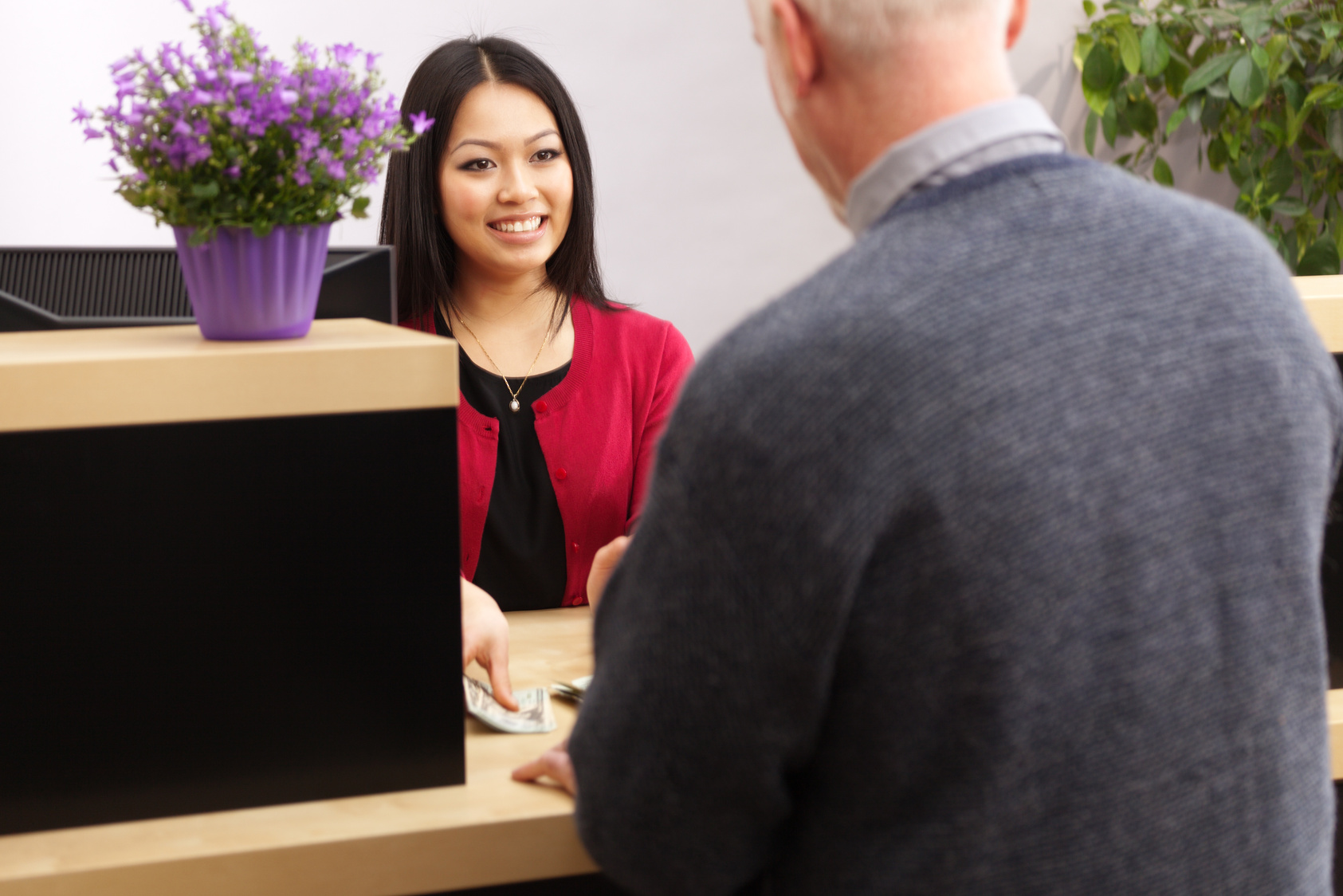 Bank Teller Serving Customer Over Retail Banking Service Counter