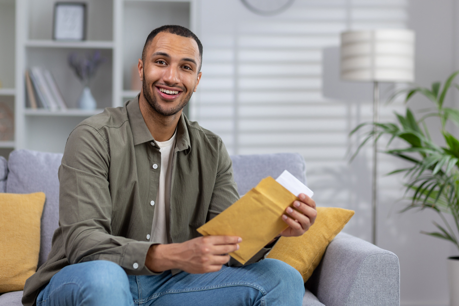 Portrait of a young Muslim man smiling looking at the camera and holding a letter, documents in an envelope delivered to his home
